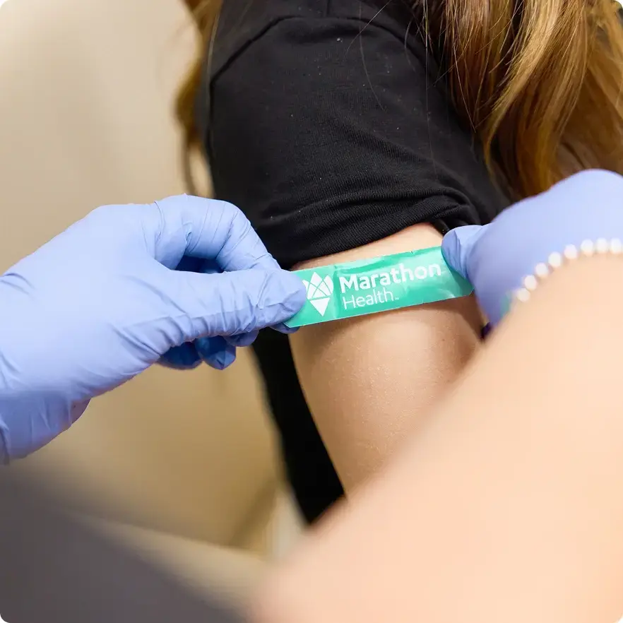 Closeup of a marathon health band-aid being applied to a persons arm.