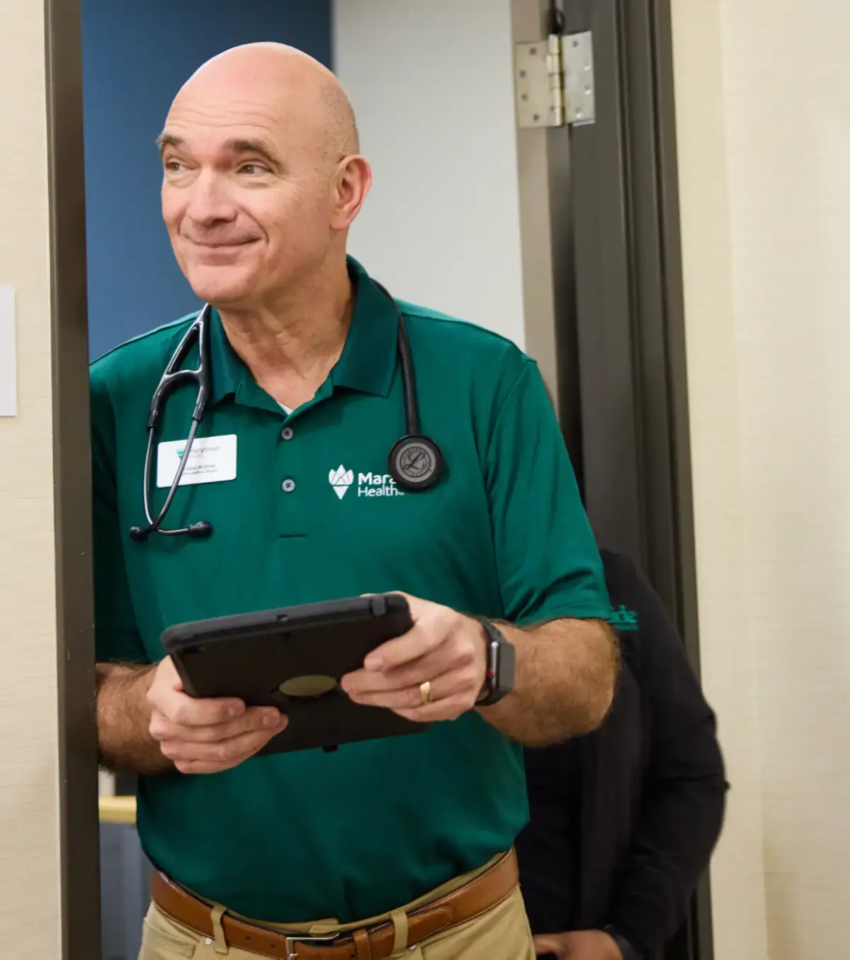 Healthcare practitioner standing in a doorway holding a tablet device.