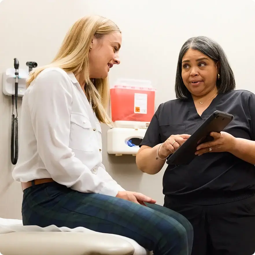 Healthcare provider speaking with a patient while pointing to health data on a tablet device.