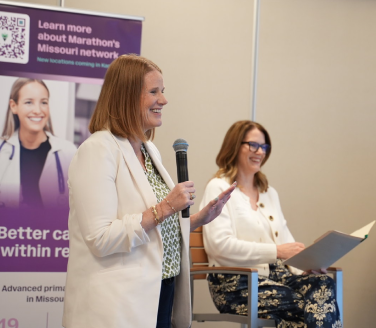 A speaker addresses a Marathon Health panel in Kansas City as Kansas City Business Journal Publisher Stacie Prosser listens.