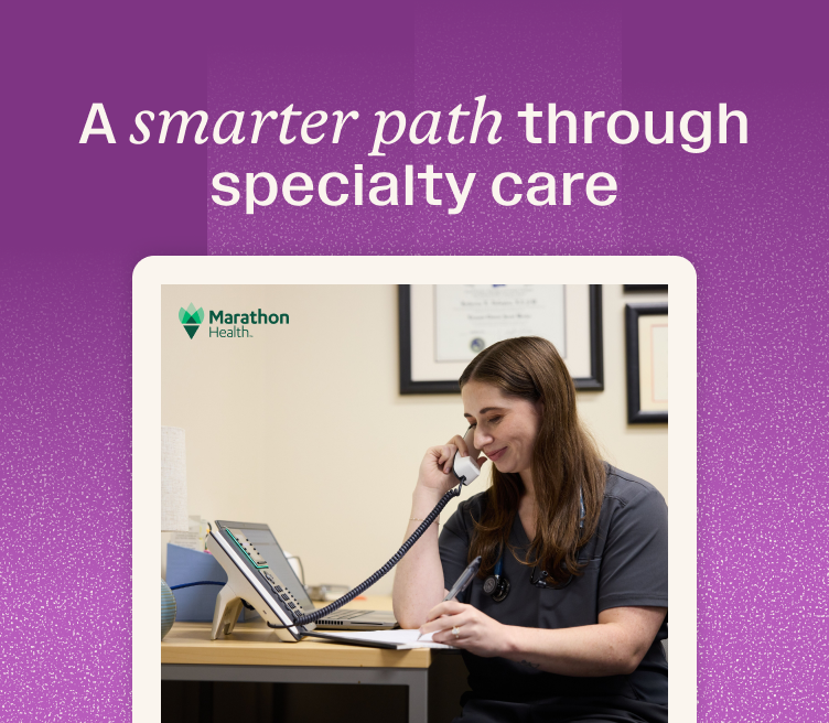 Healthcare provider in scrubs takes notes on a clipboard during a phone call, coordinating a specialty care referral from primary care