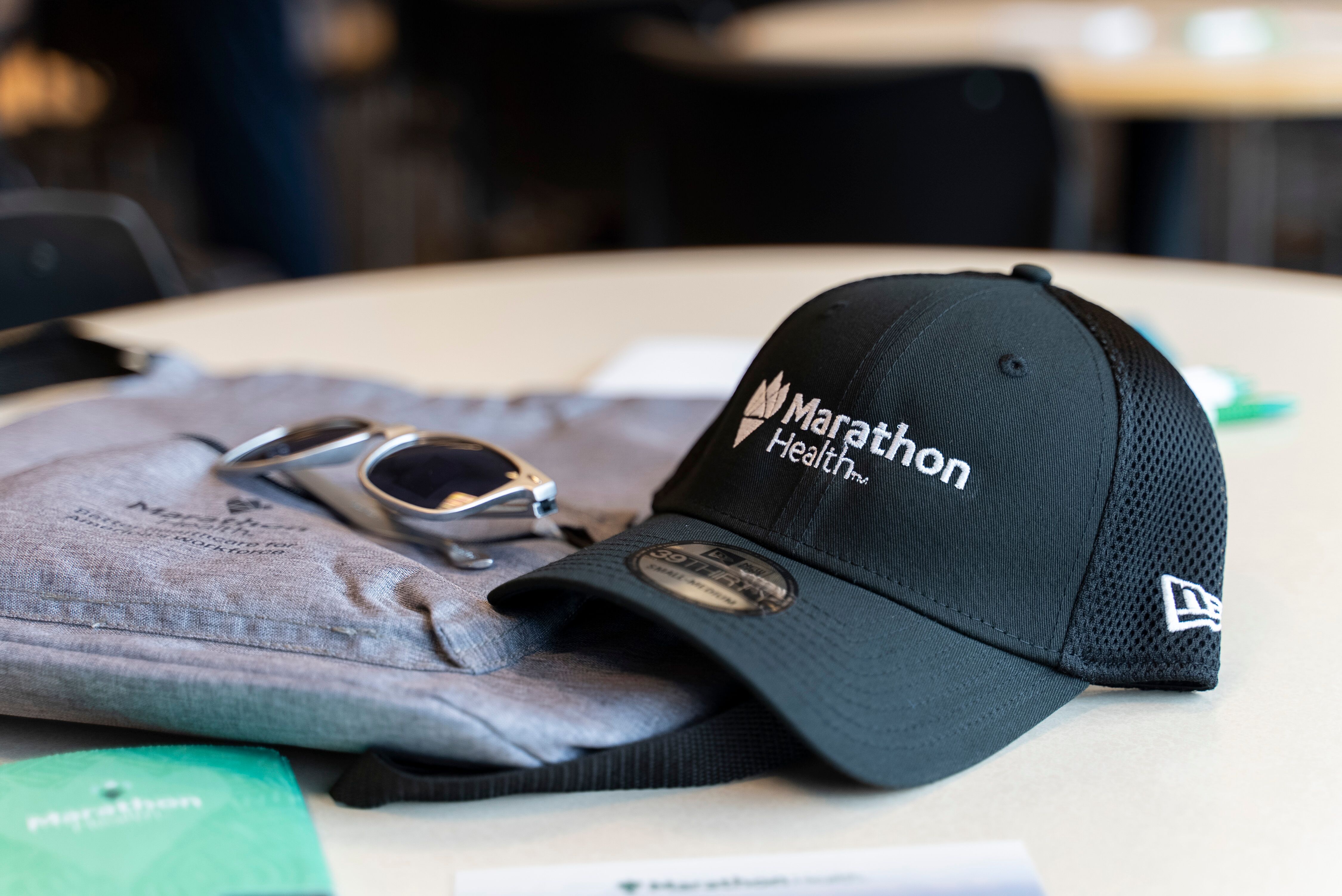 Marathon Health branded cap, sunglasses, and event swag on a table.
