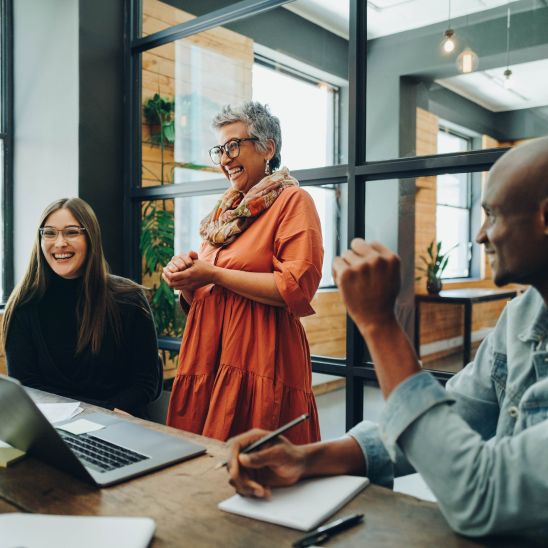Coworkers collaborating and laughing together around a table in a modern office.