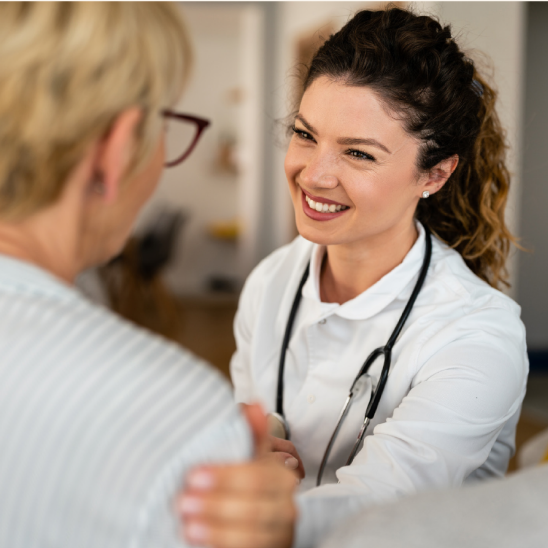A smiling healthcare provider with a stethoscope engages warmly with a person during a one-on-one conversation.