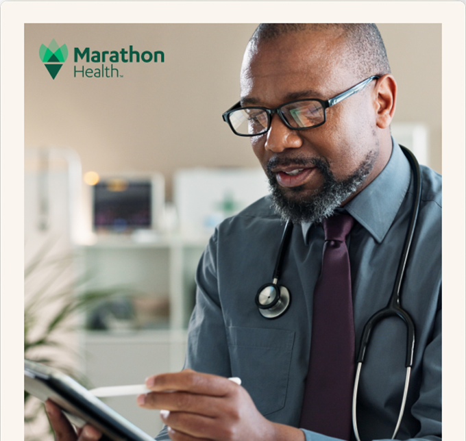 A Marathon Health physician reviews information on a tablet in a clinical office setting.