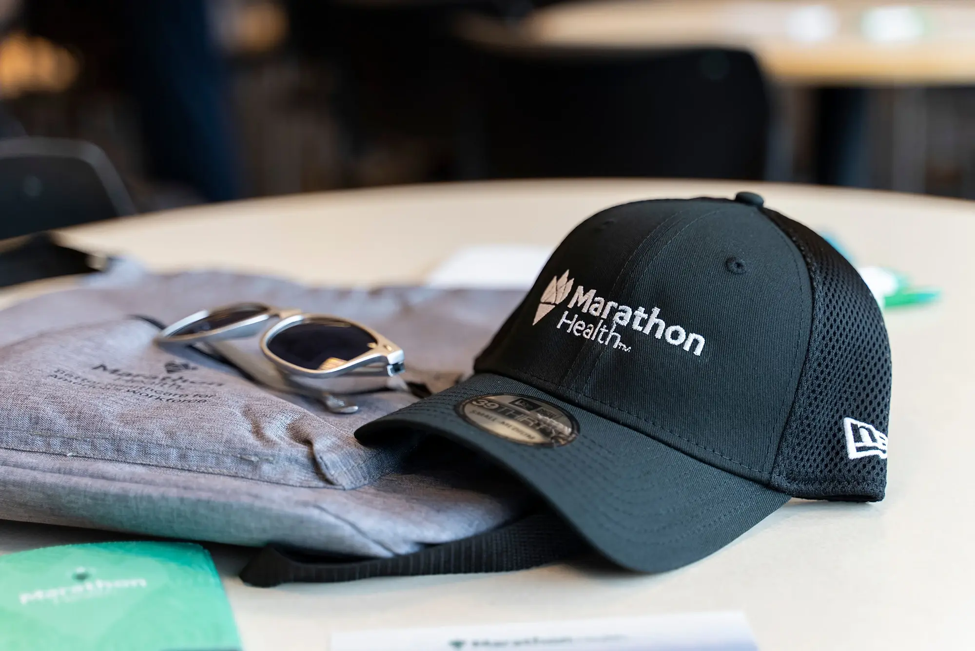 Marathon Health branded cap, sunglasses, and event swag on a table.