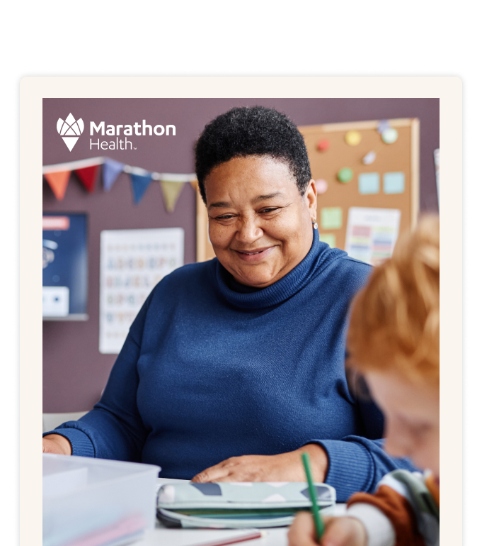 A smiling adult in a blue sweater at a classroom table with a child.